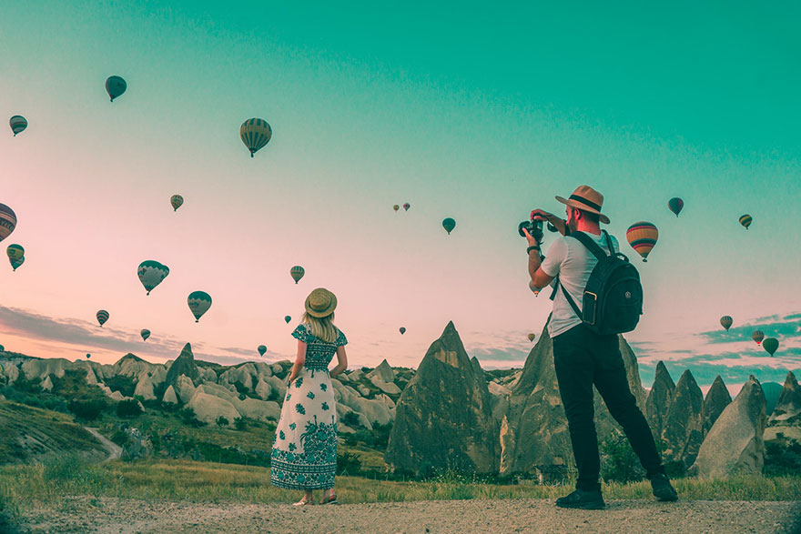 Photographer taking a picture of a woman with several hot-air balloon mid air