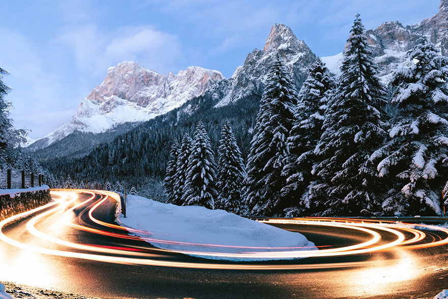 streaking lights on a cruved road with snow capped mountains