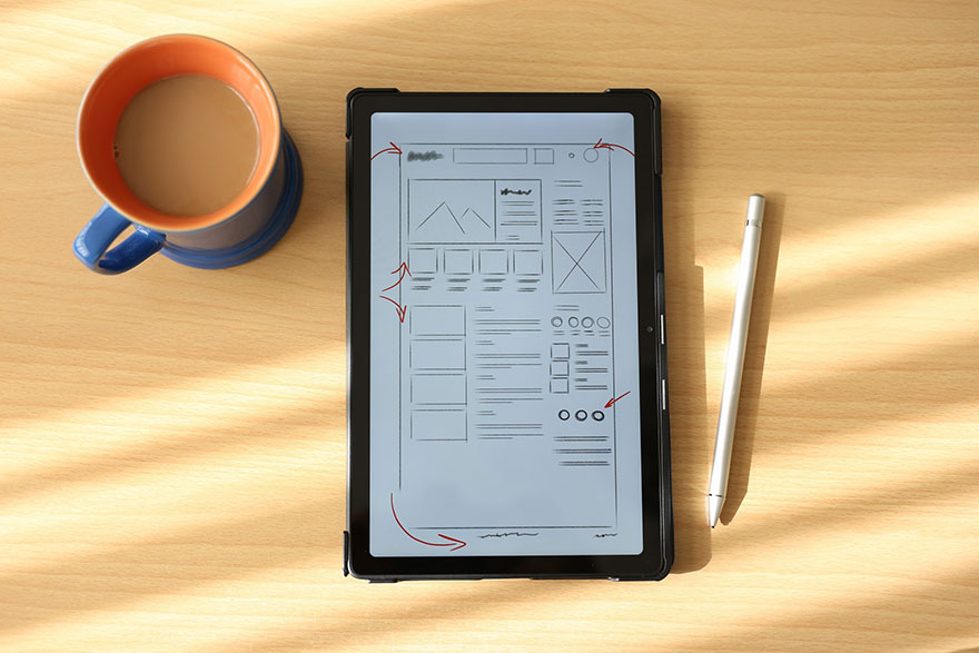 a design draft on a tablet on top of a table beside a coffee mug with coffee