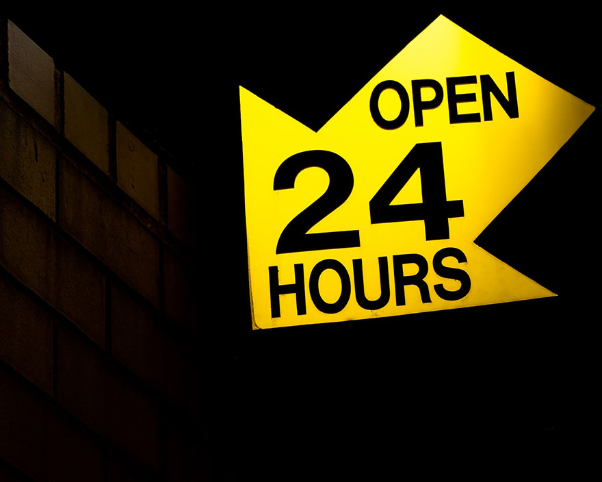 Yellow arrow shaped sign that reads open 24 hours
